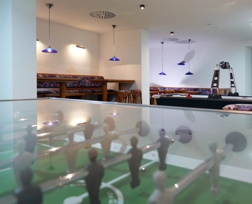 Teenieklub mit Airhockeytisch im Vordegrund und Sitzgruppen