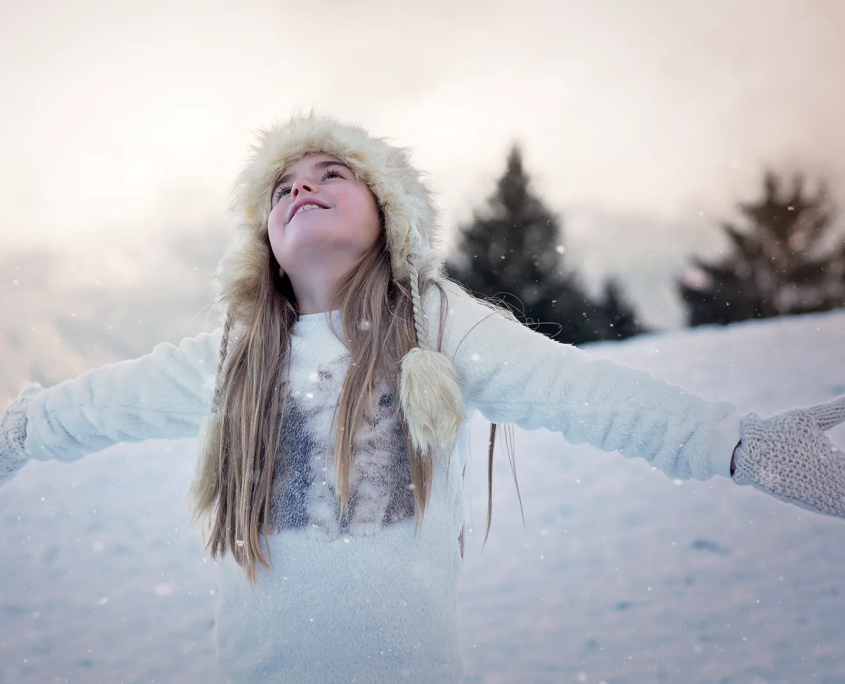Mädchen steht mit ausgebreiteten Armen in Winterlandschaft